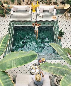 an aerial view of a pool surrounded by chairs and plants with a woman in the middle