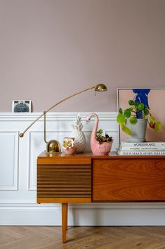 a wooden table topped with a lamp next to a pink wall