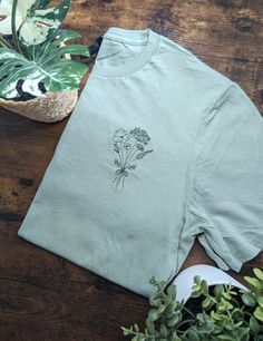 a green t - shirt with flowers on it sitting next to a potted plant