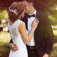 a bride and groom kissing each other in front of the sun shining through the trees