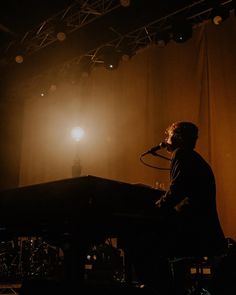 a man standing in front of a piano on stage with lights shining from behind him