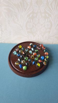 a wooden tray with many glass beads on top of blue cloth next to wallpaper