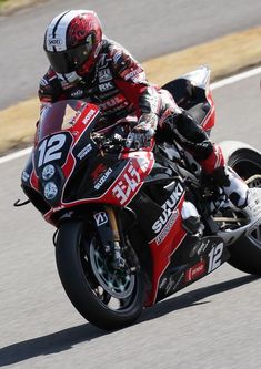 a man riding on the back of a red motorcycle down a race track in front of another person