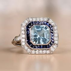 This platinum ring features a 1.97 carat aquamarine in an Asscher cut. It is surrounded by a halo of calibrated French cut sapphires, as well as a second halo of round brilliant cut diamonds. Additional round brilliant cut diamonds adorn the shoulders. The total weight of the diamonds is approximately 0.51 carats. This ring is embellished with fine milgrain and an open-work under-gallery.
The approximate dimensions of the aquamarine are 8.00mm x 8.00mm. The measurements of this ring are approxim Aquamarine Ring Vintage Eragem, Diamond Ring With Halo, Asscher Cut Diamond Ring, Asscher Cut Ring, Estate Diamond Jewelry, Ring Halo, Aquamarine Engagement Ring, French Cut, Aquamarine Jewelry