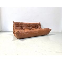 a brown leather couch sitting on top of a white floor next to a wall and window