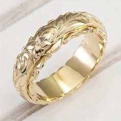 a gold wedding band with an intricate design on the outside and inside, sitting on a white surface