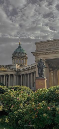 an old building with a statue in the foreground and a cloudy sky above it