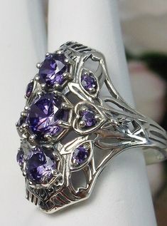 Art Deco 1930s Amethyst 9-Gem Ring9Gem Ring Design#D69 Give your wardrobe the stylish edge it needs with the Amethyst 9-Gem Ring. This stunning vintage Art Deco ring is crafted from sterling silver, making it just as timeless as its design. The piece is set with three captivating center 6mm round cut Purple/Amethyst CZ gemstones and six more 2mm gemstones that adorn the sides of the setting. A unique filigree silver band completes this work of art to perfections - an impressive reminder of the g Victorian Amethyst Ring With Accent Stones For Anniversary, Vintage Amethyst Ring With Accent Stones For Anniversary, Vintage Purple Jewelry For Anniversary, Vintage Purple Jewelry For Anniversaries, Vintage Amethyst Ring With Accent Stones, Vintage Amethyst Ring With Accent Stones For Collectors, Vintage Amethyst Ring With Intricate Design For Anniversary, Vintage Amethyst Ring With Accent Stones For Wedding, Art Deco Hallmarked Amethyst Ring For Anniversary