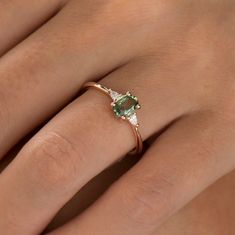 a woman's hand wearing a ring with an oval shaped green stone and diamond accents