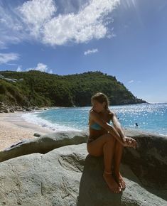 a woman sitting on top of a large rock near the ocean