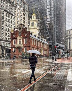 a person walking down the street in the rain with an umbrella over their head and buildings behind them