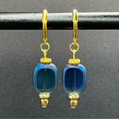 two blue glass beads are hanging from gold plated earwires on a black background