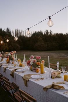 an outdoor dinner table set with candles, flowers and napkins for guests to eat