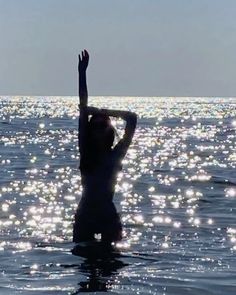 a woman standing in the water with her arms up and hands raised above her head