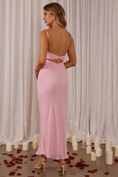 a woman standing in front of candles wearing a pink dress with open back and cut out shoulders