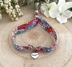 the bracelet has a heart charm on it and is decorated with colorful floral fabric, along with white flowers