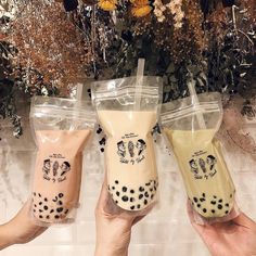 three people holding up drinks in plastic bags with black spots on them and flowers behind them