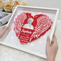 a person holding up a heart shaped paper cutout with an angel and name on it