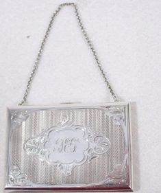 a silver purse hanging from a chain on a white wall with a monogrammed design