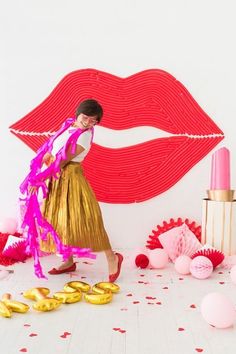 a woman in a gold skirt and pink scarf standing next to a red lips backdrop