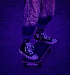 a person on a skateboard in the dark with purple lighting behind them and their feet up