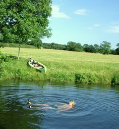 a man floating on top of a body of water next to a green field with trees