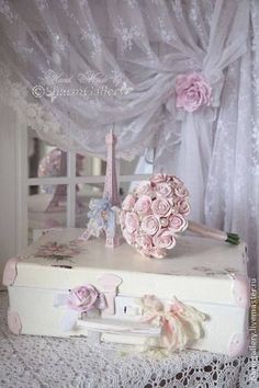 a white suitcase with pink flowers on top of it next to a lace covered window