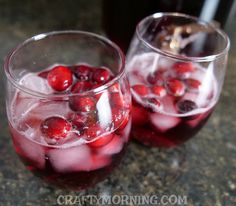 two glasses filled with ice and cranberries on top of a granite countertop