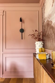 a room with pink walls and wood flooring in the center is decorated with gold vases