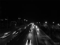 black and white photograph of traffic on highway at night with lights in the dark sky