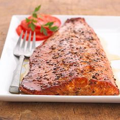 a piece of salmon on a white plate with a fork and cherry tomatoes in the background