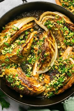 a skillet filled with cooked onions and green garnish on top of a table