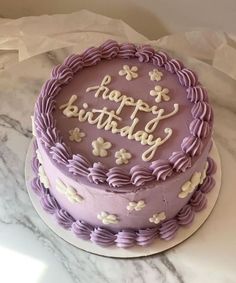 a birthday cake with purple frosting and white flowers on the top that says happy birthday