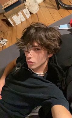 a young man sitting on top of a couch next to a wooden floor covered in clutter