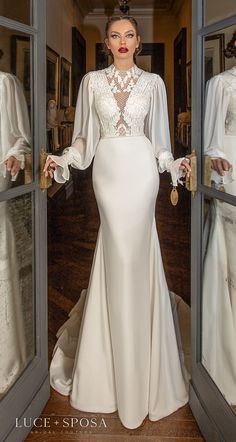 a woman standing in front of a mirror wearing a white dress with sheer sleeves and long sleeves