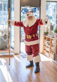 a man dressed as santa claus standing in front of a store window with his arms outstretched