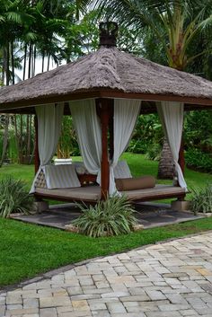 a gazebo sitting in the middle of a lush green yard with white drapes