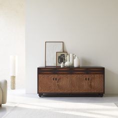 a wooden cabinet with two vases sitting on it's sideboard in front of a white wall