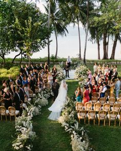 an outdoor wedding ceremony at the beach with lots of people sitting on chairs and facing the water