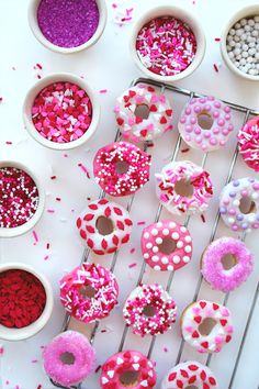 pink and white donuts with sprinkles in bowls next to them on a rack