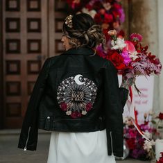 a woman wearing a black leather jacket and white dress is standing in front of flowers