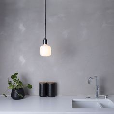 a white sink sitting next to a black vase on top of a counter under a light fixture