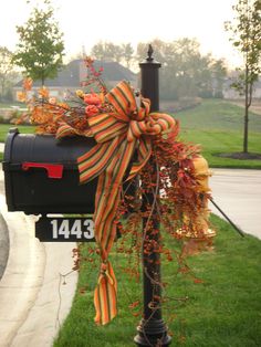 a mailbox decorated with an orange and yellow bow is sitting in the grass next to a lamp post