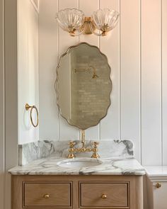 a bathroom vanity with marble counter top and gold faucet, two lights above it