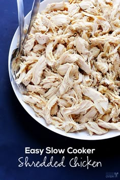 a white bowl filled with shredded chicken on top of a blue tablecloth next to a fork