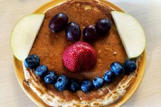 pancakes with fruit on top and face made to look like an apple, blueberries, and raspberry