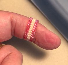 a person's hand with a pink and white beaded ring on their finger