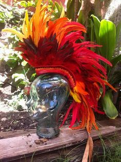 a red and yellow headdress sitting on top of a wooden table next to plants