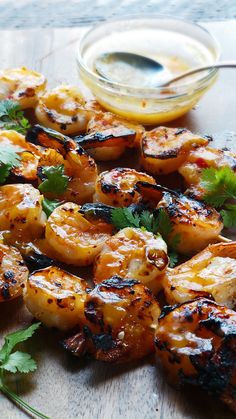 grilled shrimp with cilantro and parsley on a wooden board next to dipping sauce