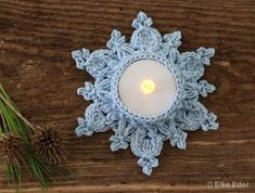 a crocheted snowflake candle holder with a lit candle